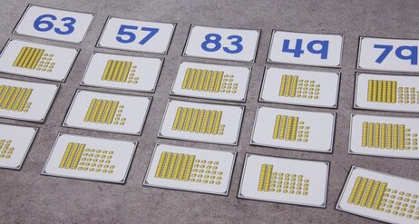 Photo shows cards with yellow place value blocks sorted by the numeral they represent. Some cards have more than ten ones-blocks.