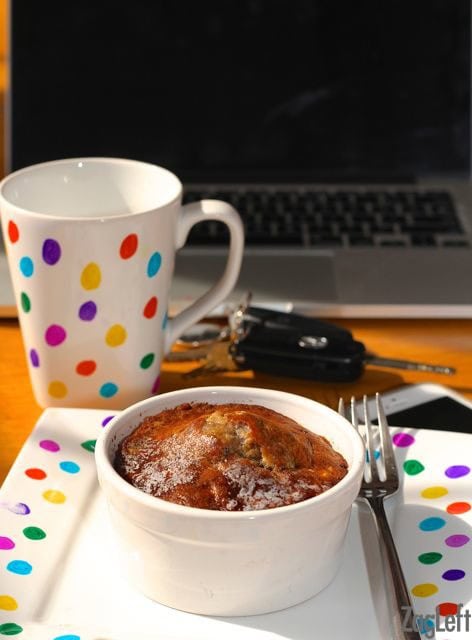 Banana bread in a small ramekin on a plate with rainbow polka dots next to a matching coffee much and a laptop computer