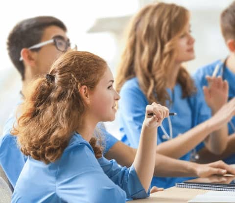 Medical assistant students in blue scrubs learn in a classroom.