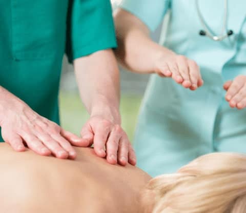 Massage therapy student in green scrubs learns technique from an instructor in mint-green scrubs.