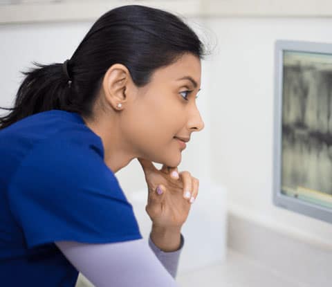 Woman in medical scrubs with a ponytail looks at an x-ray.