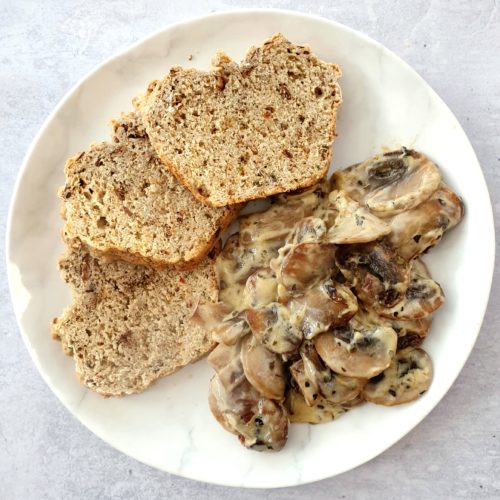 Close cropped overhead shot of mushrooms on a white plate with 3 arranged slices of soda bread.