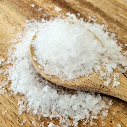 Close up of sea salt spilling off a wooden spoon onto a wooden board.