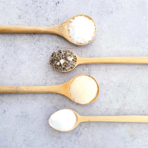 4 wooden spoons on a pale background each with a different type of salt. 2 spoons each come into the frame from the left and the right.