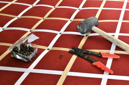 box of decorative nails, rubber mallet, and wire cutters adjusted on top of picture board