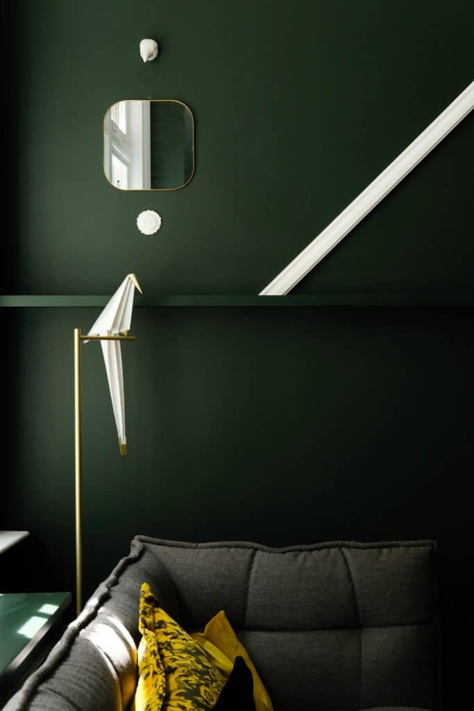 Dettaglio di un soggiorno con pareti verde scuro, angolo di divano in tessuto grigio e cuscino giallo.