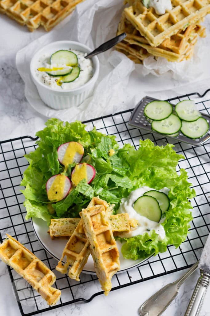 Zucchiniwaffeln mit Zaziki 4 Zucchiniwaffeln in Streifen geschnitten mit Zaziki, Salat und Gurkenscheiben angerichtet