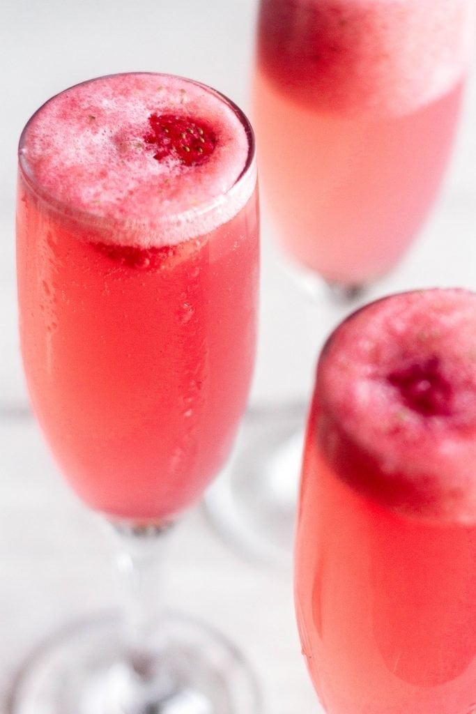 The rossini cocktail is your new favorite brunch drink! Made with strawberry puree, sparkling wine, and simple syrup. angled shot of strawberry bellini rossini cocktail on white marble