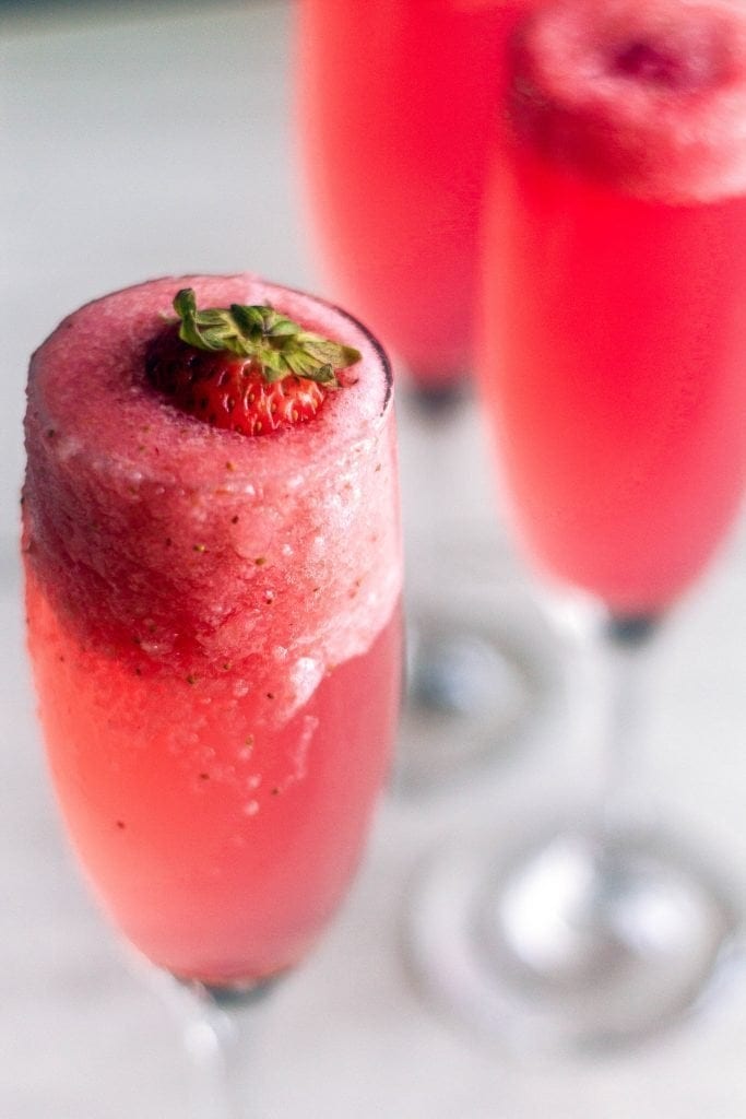 The rossini cocktail is your new favorite brunch drink! Made with strawberry puree, sparkling wine, and simple syrup. angled shot of strawberry rossini with foam flowing over the champagne flute
