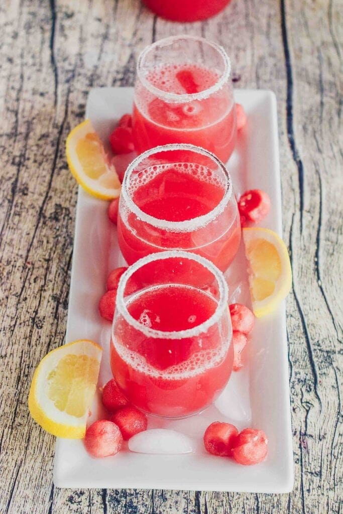 three glasses of watermelon agua fresca on a long rectangular platter with melon balls and ice