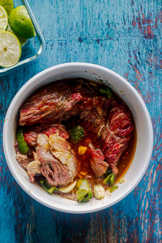 meat being marinated in a bowl of carne asada marinade
