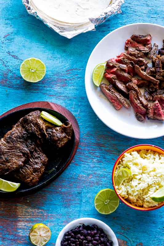 authentic mexican carne asada prepared for tacos with rice, limes slices, and tortillas