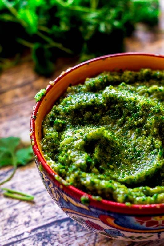 A bowl of homemade puerto rican sofrito on a wood table with cilantro in the background