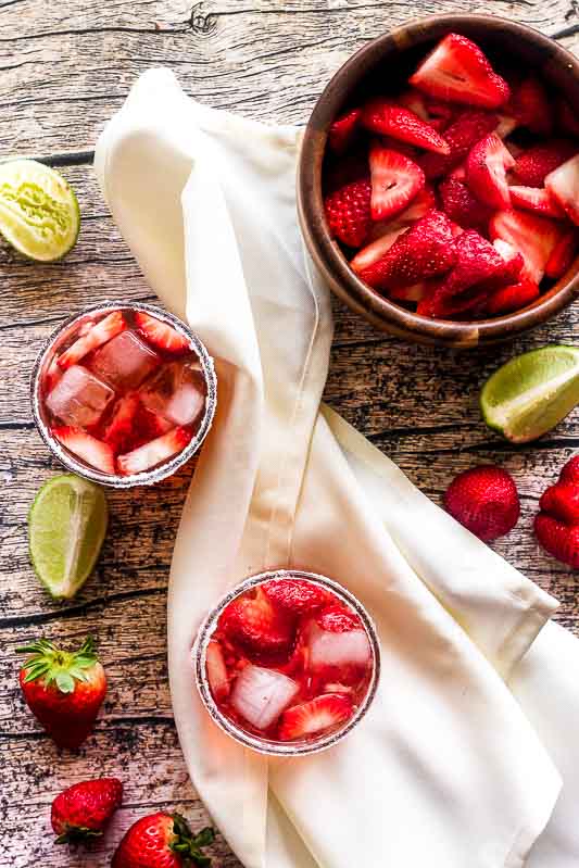 strawberry gin smash overhead with limes and a bowl of strawberries on wood