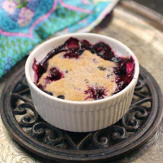 a small blueberry cobbler baked in a white dish on a trivet placed on top of a silver tray.