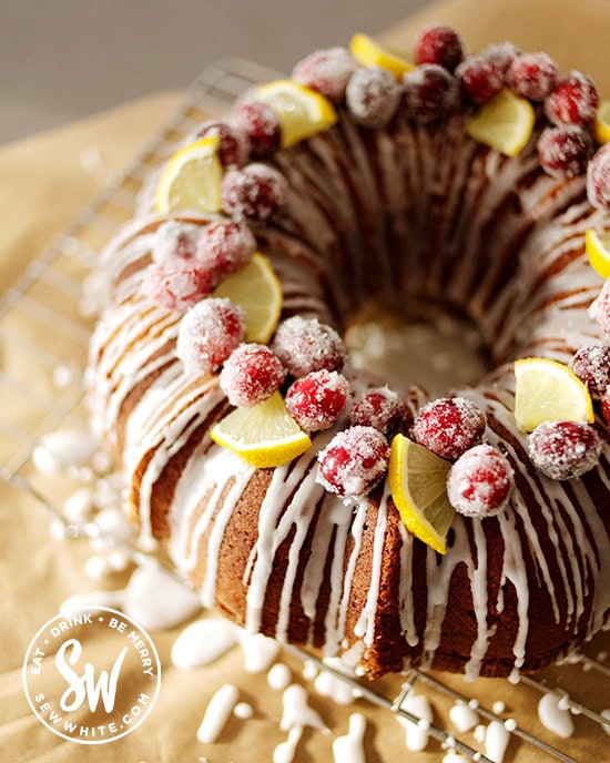 sugar dusted cranberries and lemon slices on top of a golden brown bundt cake drizzled with white icing