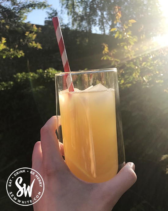 A tall glass of White Rum Pineapple Cocktail with red and white stripe straw in the sunshine.