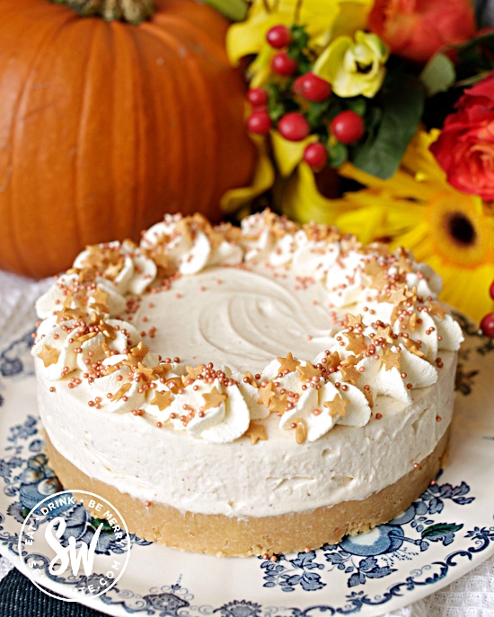 The finished pumpkin spice cheesecakeon a blue and white plate with a pumpkin and flowers in the background.