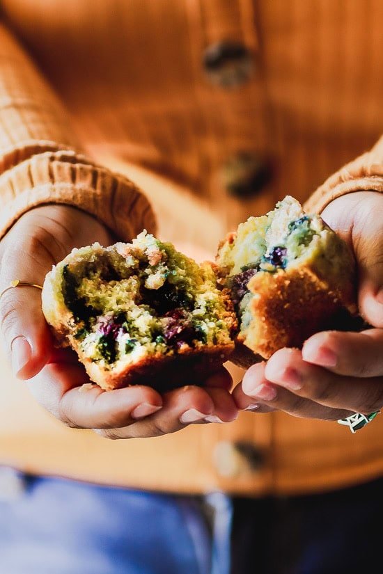 a blueberry muffin split in half being held in hands