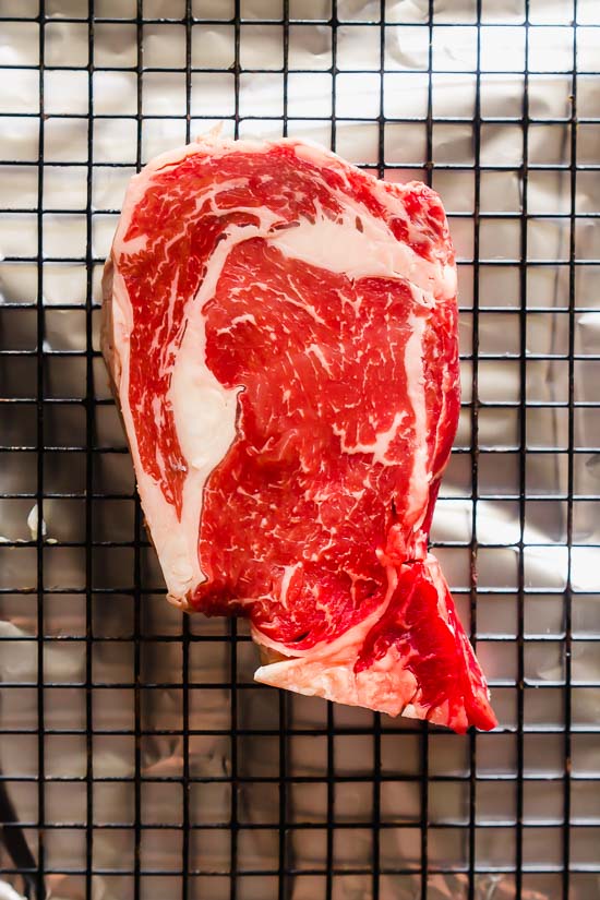 a raw well marbled rib eye steak on a wire rack