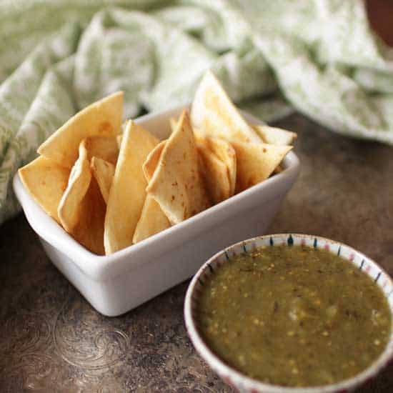 Baked Tortilla Chips in serving dish with green salsa in a bowl