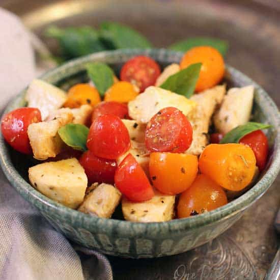 caprese salad in a green bowl on a silver tray next to a brown napkin.