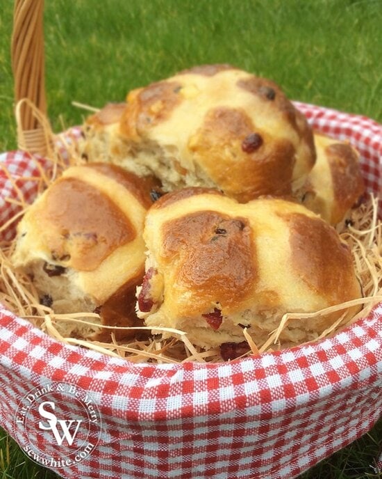 Cranberry and Lime Hot Cross Buns in a wicker basket on straw for Easter.