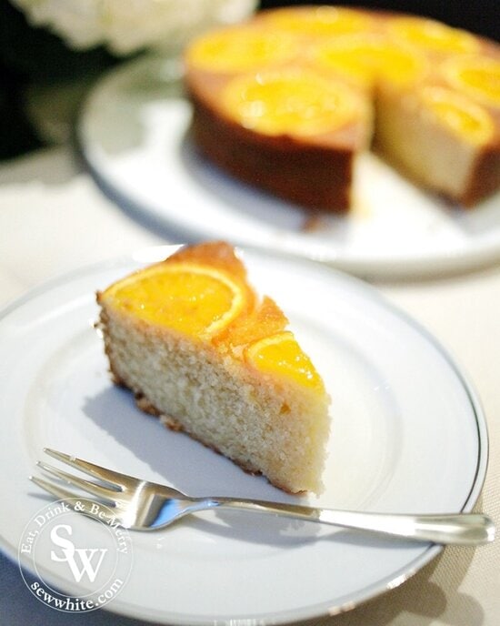 A golden orange sponge slice ready to enjoy with silver pudding fork decorated with slices of orange.