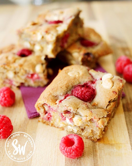 Golden brown gorgeous studded raspberry white chocolate cookie traybake surrounded with fresh raspberries.