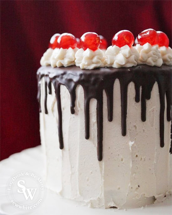 A Easy Black Forest Cake topped with dripping chocolate and glace cherries