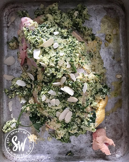 pesto chicken with almonds and parsley rubbed in to a chicken in a silver baking tray ready to be cooked.