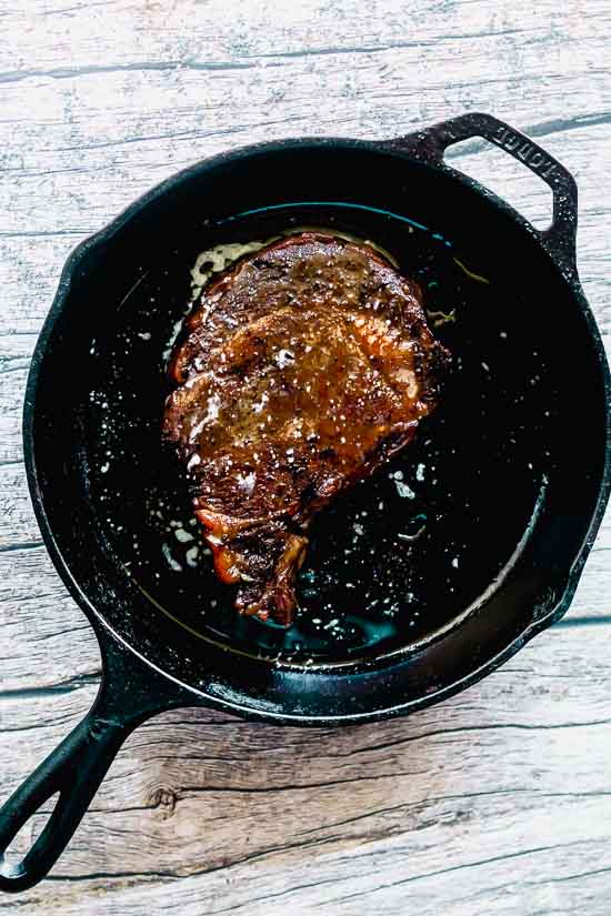 overhead shot of a reverse seared steak in a cast iron pan, basted with butter