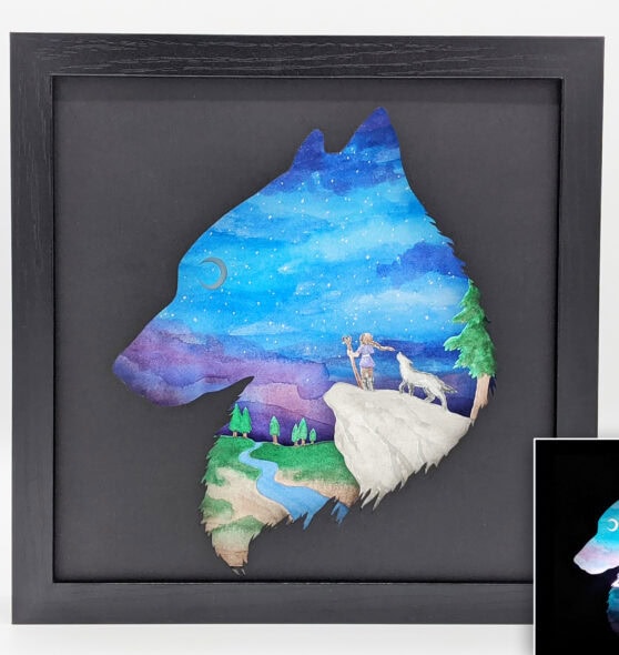 Hand cut paper art of a wolf and a girl standing on a rock looking out over a valley at the moon in the distance.