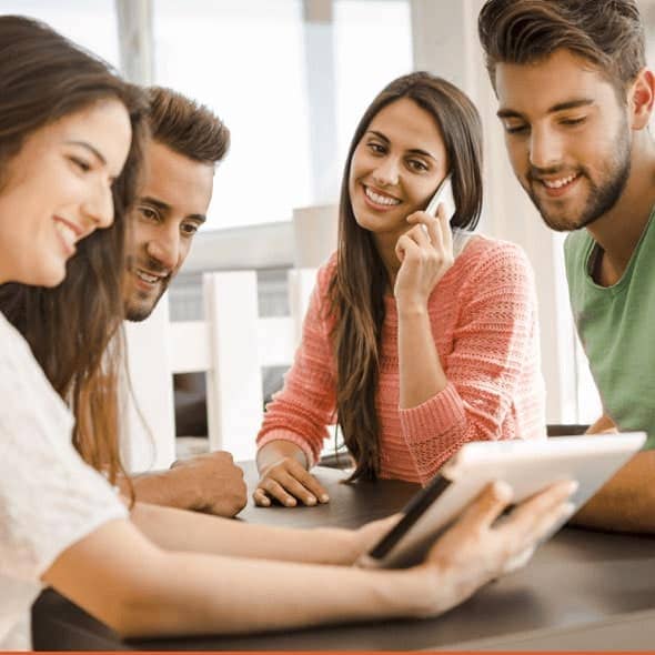 Group of happy young people look at something on an iPad while one woman talks on the phone.