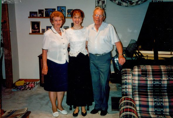 Kristen and her grandparents standing by a piano