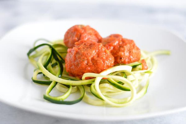 Meatless balls made with eggplant on top of zucchini noodles on a white plate.