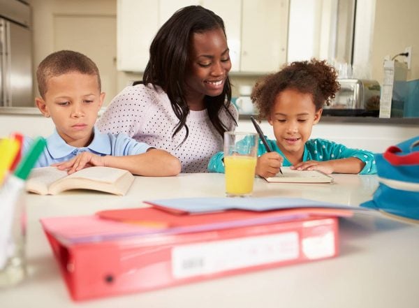 mum doing homework homeschooling mother sitting at table with her children doing homework