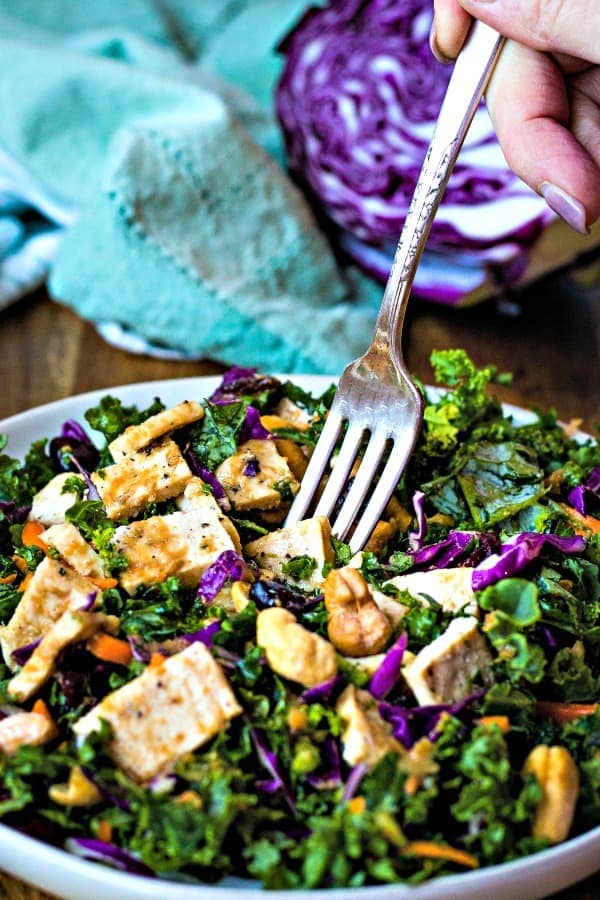a fork spearing a piece of chicken in a bowl of salad