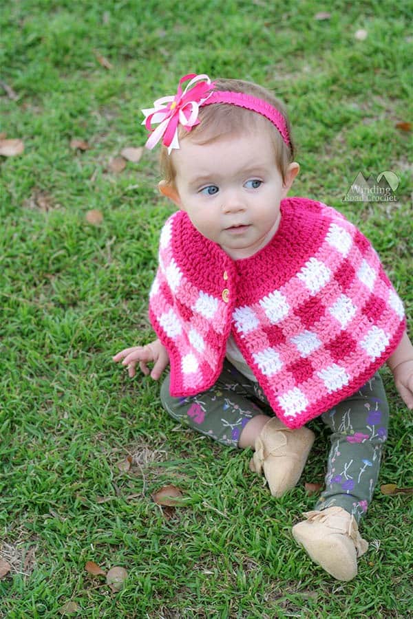 A crochet plaid cape is the perfect accessory to a spring baby dress. This free crochet pattern uses only basic stitches and works up quick and easy. Baby, toddler, and girl size patterns. #freecrochetpattern #plaidcrochet #crochetcape
