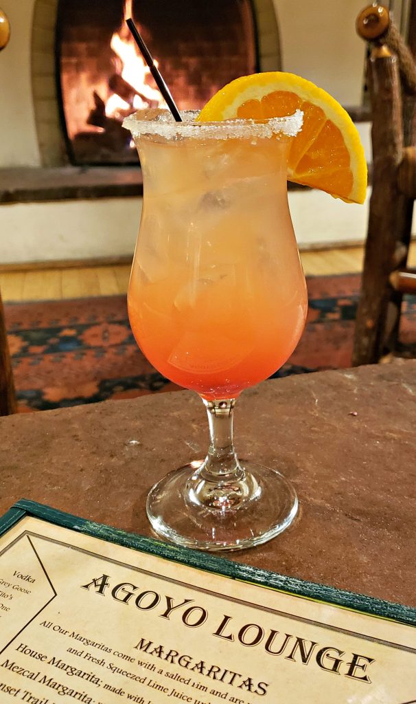 Margarita in hurricane glass sits on table in front of fireplace - colors are like the sunset