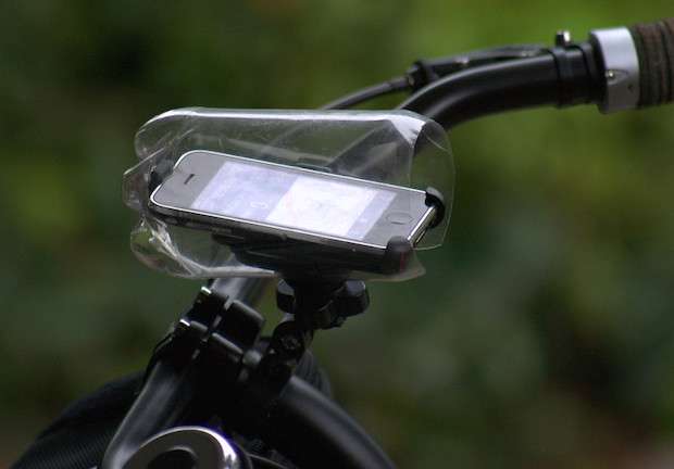 An iPhone mounted in bike handlebars, with the bottom half of a plastic pop bottle covering it for rain protection
