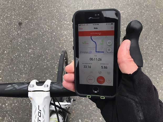 Closeup of a cyclist holding an iPhone above the handlebars with the Strava app running