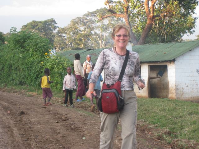 Smiling Unstoppable Stacey walks on dirt road while family looks on from their one-story