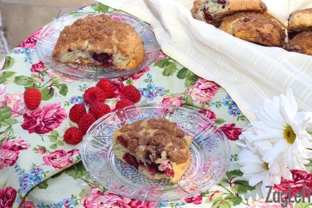 A small basket filled with scones and two scones plated on a floral napkin near a handful of raspberries