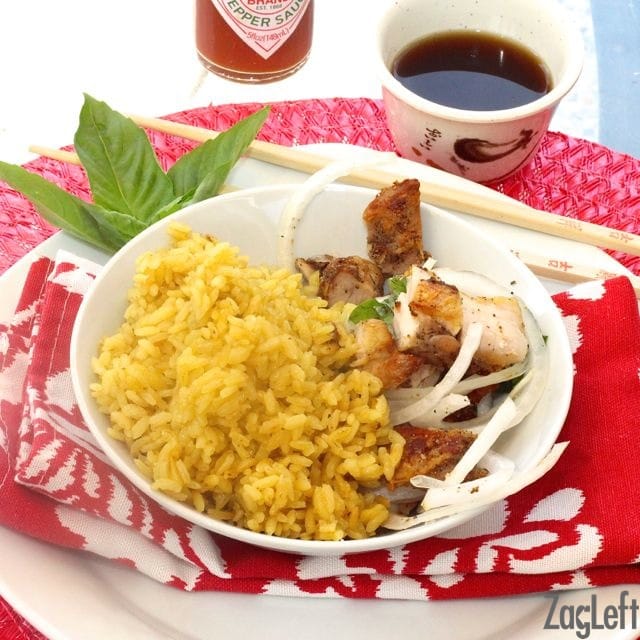 Chicken and golden rice with slices of onions in a bowl with chop sticks and soy sauce in a small bowl