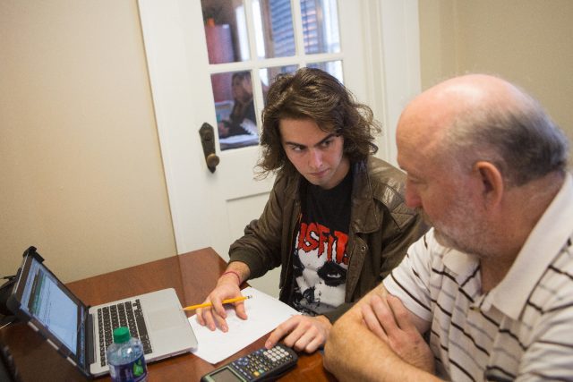 Student and tutor sit at table with a laptop with pencil and paper.