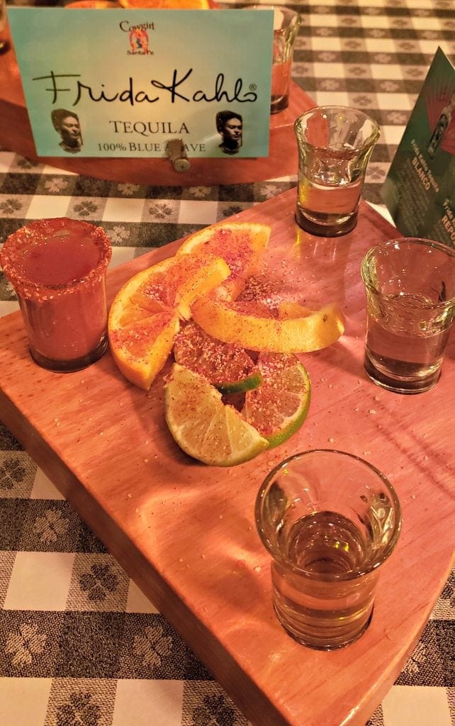 Three shot glasses of tequila sit on diamond-shaped board with a shot glass of tomato juice with spiced salt rim