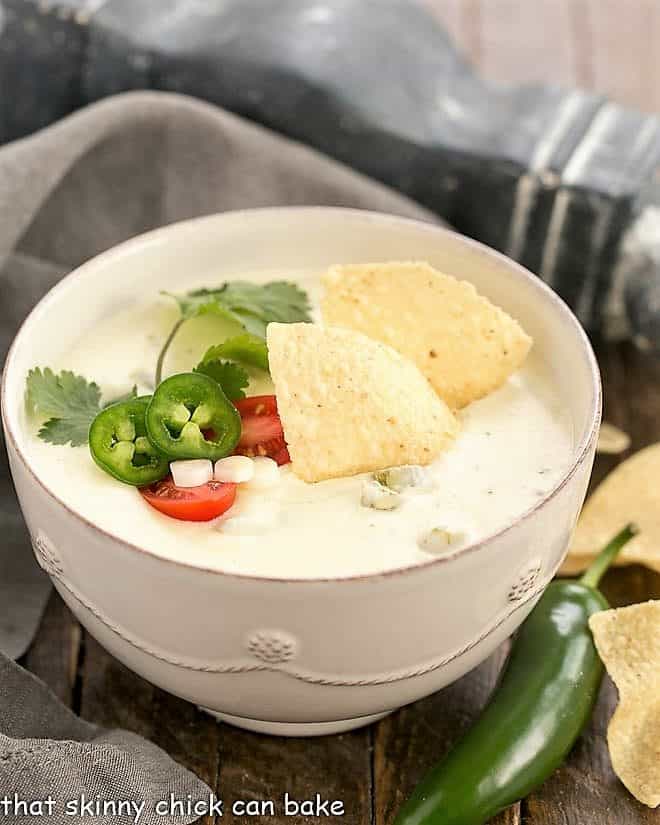 Easy Homemade Queso Dip - thick, creamy, cheesy with the perfect amount of heat! Served with tortilla chips, this Tex-Mex dip will disappear in a flash!!! Easy Homemade Queso Dip in a white serving bowl topped with tortilla chips, jalapeno slices, cilantro sprig