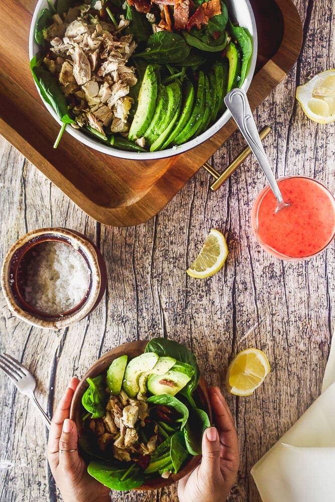 overhead of chicken bacon avocado salad in a large serving bowl and in a small wooden bowl with strawberry vinaigrette