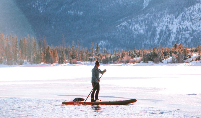 Paddleboarding is done with a paddle on all kinds of water Person stand up paddle boarding on a frozen lake in the mountains